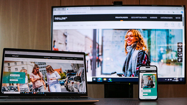 Ein großer Bildschirm, ein Laptop und ein Mobiltelefon mit drei Bildmotiven der neuen Webseite. 