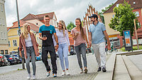 fünf fröhliche Frauen und Männer gehen mit Handys in der Hand eine Straße  in Neubrandenburgs Innenstadt entlang