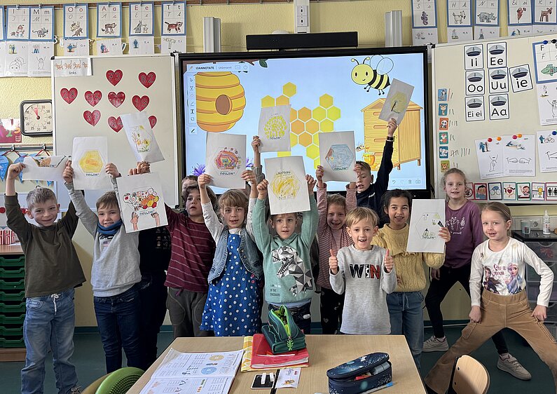 Gruppenfoto: Im Klassenraum halten die Kinder der neu.sw Patenklasse ihre bunten Bilder von Bienenwaben in die Höhe. 