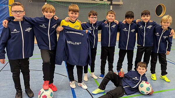 Mannschaftsbild eines E-Junioren-Teams des FCN. Die Jungen tragen lange schwarze Trainingshosen und dunkelblaue Trainingsjacken mit Vereinslogo sowie weißem neu.sw Aufdruck. 