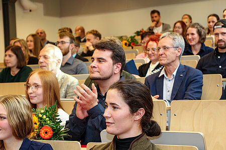 Mneschen in einem Hörsaal aitzend.