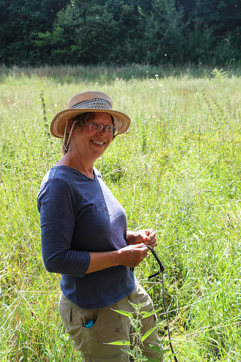 Angelika Fuß vom NABU steht lächelnd auf der blühenden Wiese. Sie trägt einen Sonnenhut.