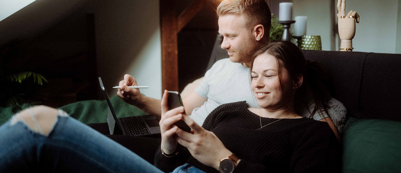 Ein Pärchen auf der Couch mit Handy und Tablet 