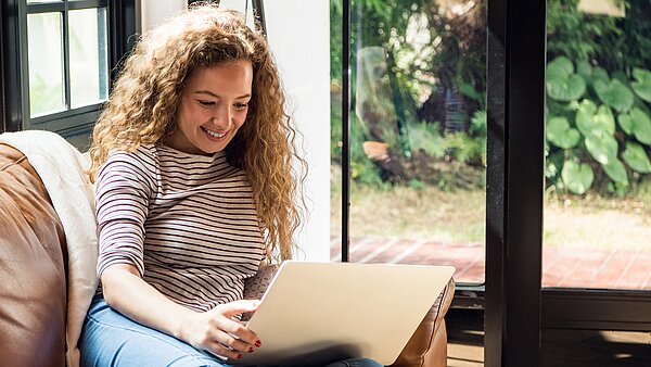 Frau sitzt mit Laptop auf der Couch