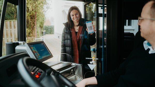 Junge Frau zeigt beim Einsteigen in den Stadtbus ihr E-Ticket beim Fahrer vor. 