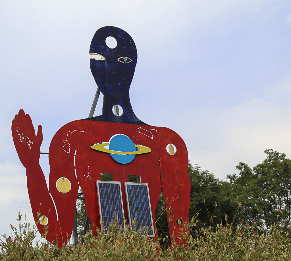 Skulptur eines Außerirdischen mit Solarzellen auf der Brust und zum Gruß erhobener Hand.